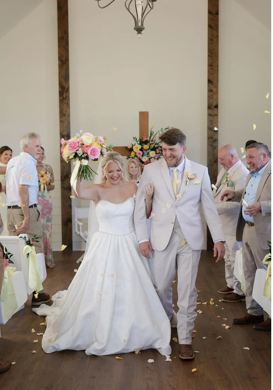 Newlyweds walking out through falling flower petals at Gateley Hill Gardens